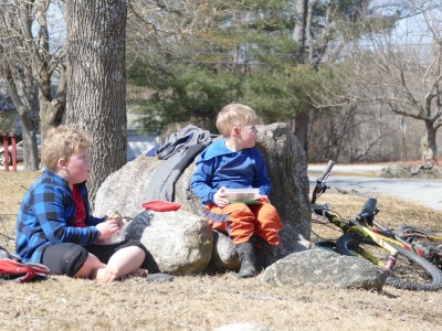 Harvey and Zion picnicing by a small boulder in a mown field