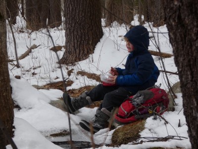 Elijah eating lunch on a snow-free rock by a pond
