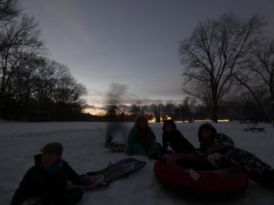 the boys and friends pausing at the top of a sledding hill at dusk