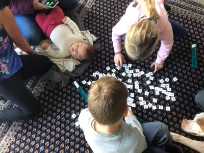 Lijah working with letter tiles on the floor with mamas, baby, and dog nearby