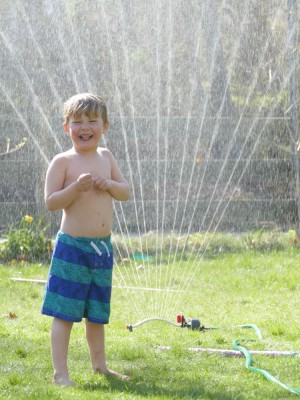 Lijah in swimsuit standing under the sprinkler