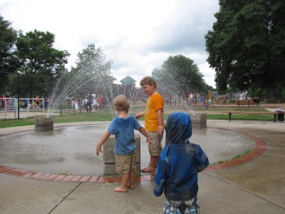 the boys, a little wet, in front of a spray-park fountain