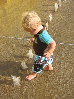 Lijah playing with the little fountains in the spray park