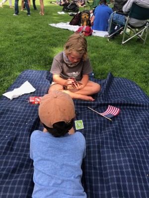 Elijah playing Uno with a friend on a picnic blanket, a little American flag alongside him