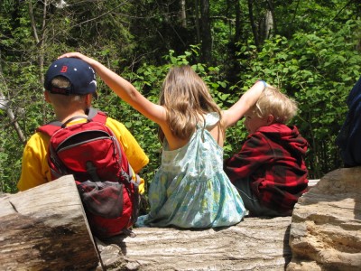 Harvey, Taya, and Zion sitting on a log, Taya putting her hands on the boys' heads