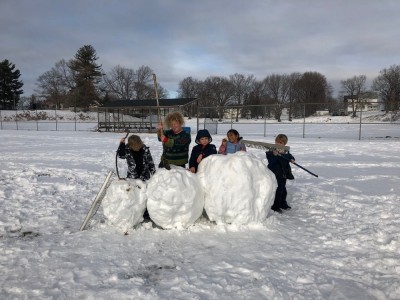 kids posing with a giant recumbant snowman they made, pretending to have killed it