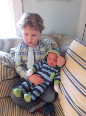 Harvey sitting on the couch holding Elijah on his lap; both wearing blue and green
