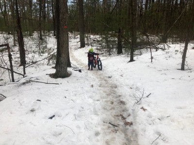 Elijah pushing his bike uphill on a snowy trail