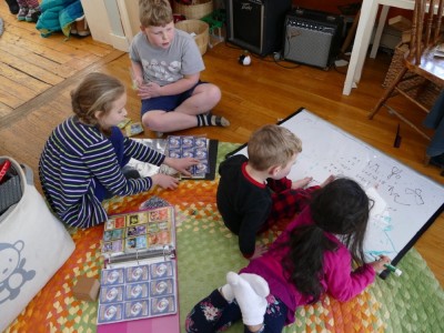 kids on the floor looking at Pokemon cards and drawing on the whiteboard