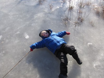 Zion lying on his back on the pond ice, making an ice angel