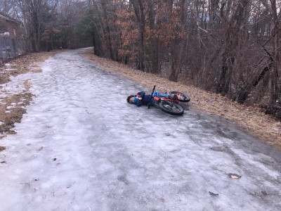 Elijah lying under his bike on a big patch of ice on the bike path