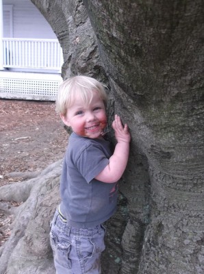 Zion, with ice cream on his face, smiling while hugging a tree