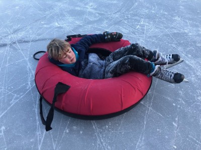 Elijah, covered in ice dust, lying in a snow tube on the ice