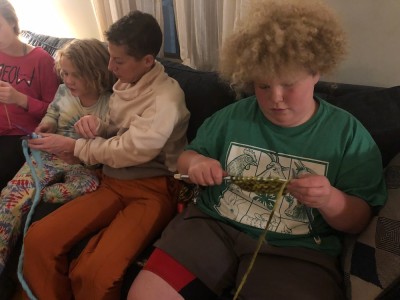 Leah sitting on the couch with Harvey and Elijah, teaching them how to knit
