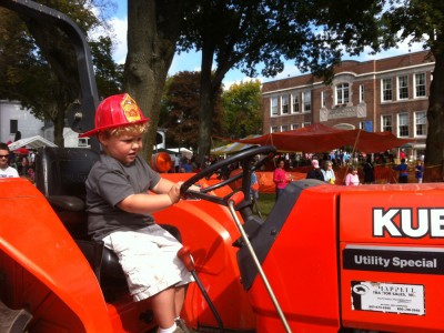 Harvey in the driver seat of a tractor, still wearing the fire hat