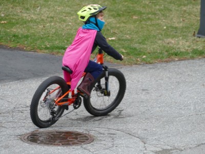 Elijah riding his bike wearing a pink cape