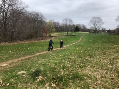 Harvey and Zion riding on a singletrack path through a field