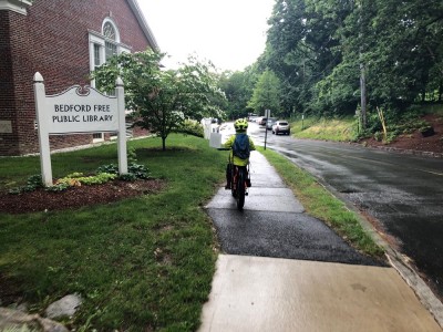Elijah riding his bike to the library doors in the rain