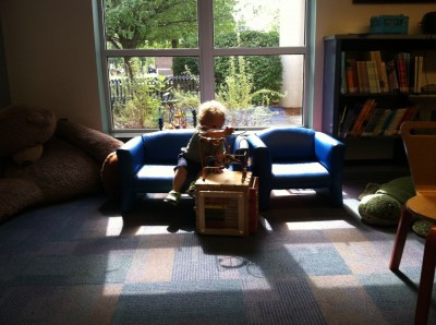 Lijah sitting on the little couch in the kids room, lot from behind by the window, playing with toys