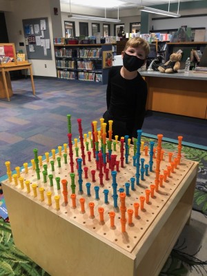 Elijah standing by the creation he made with peg toys at the library