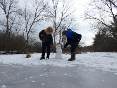 Harvey and Zion putting the finishing touches on a two-foot-tall snowman on a frozen pond