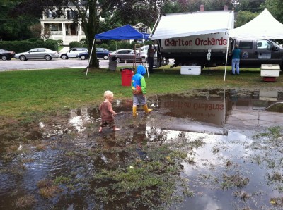 Harvey and Elijah walking through a giant puddle on the grass at the farmers market