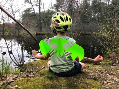 Elijah in meditation pose by a pond, wearing paper wings