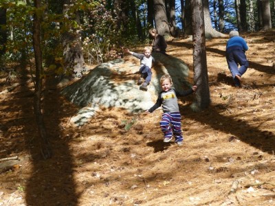 the boys and a friend sliding down a rock on a woodsy hillside