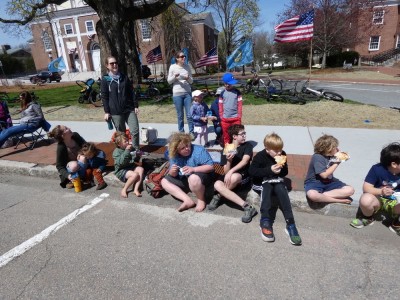 the kids sitting on a curb with friends waiting for the parade