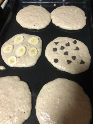 pancakes cooking on the griddle: four plain, one chocolate chip, one banana