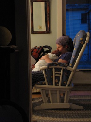 Leah holding Lijah in the rocking chair, lit by one lamp in the otherwise dark house
