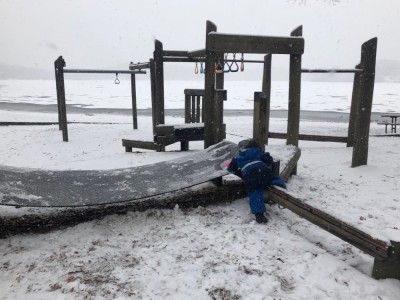 a toddler climbing on a snowy playground structure in falling snow
