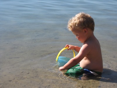 Lijah sitting in shallow water with a bucket