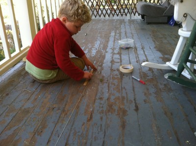 Harvey sitting on the porch floor using a ruler to measure distance on a string