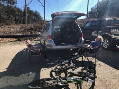 Harvey and Elijah sitting by the open trunk of the car, near their bikes
