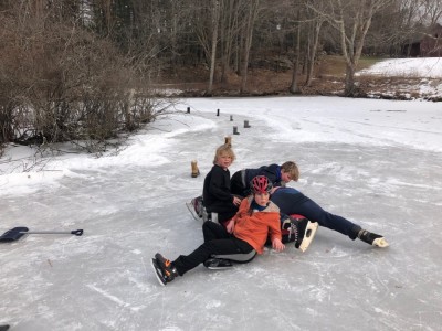the boys and friends lying on a sled on the mostly-shoveled ice of a little pond