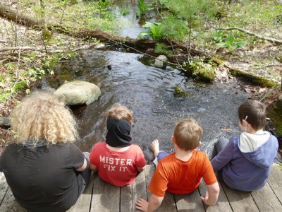 the boys and a friend sitting on the edge of a bridge over a stream