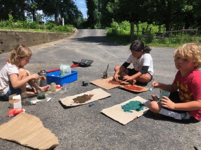 Elijah and friends sitting on a driveway making colored sand