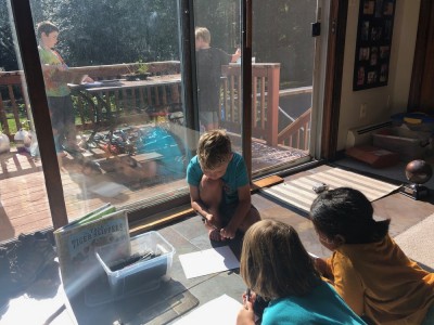 Elijah drawing with friends inside a sliding door, Zion painting out on a deck