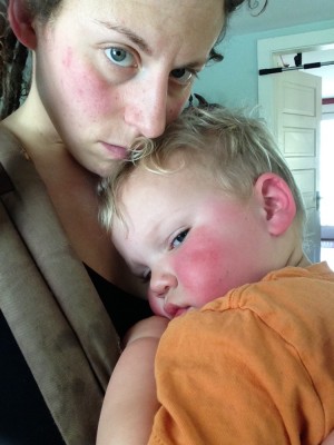 Mama holding a red-faced sick-looking Lijah in the ergo