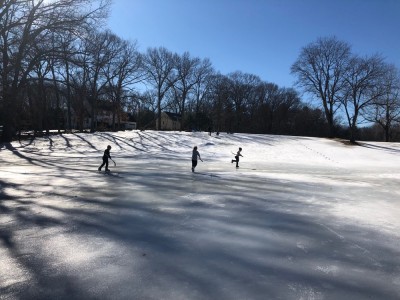 boys playing hockey on ice at the base of the sledding hill