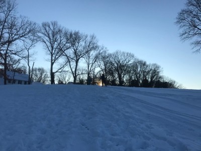 sledders at the top of the hill with the low sun behind them