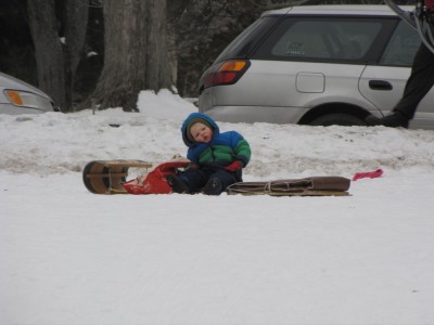 Lijah sitting on the toboggan, about to fall asleep and fall over