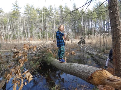 Elijah eating from a tupperware while standing on a fallen log over a pond