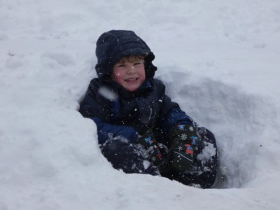 Elijah sitting in a tiny snow fort in the falling snow