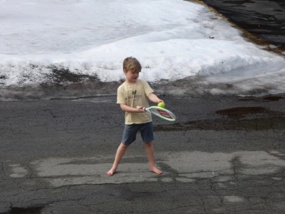 Elijah, barefoot and in shorts, playing with a tennis racket on the street