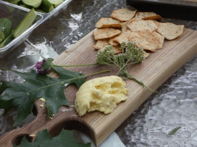a cutting board beautifully laid with cheese, crackers, flowers, and oak leaves