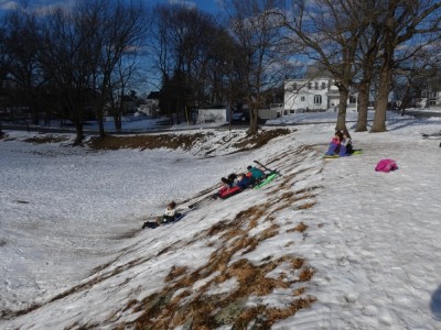 kids sledding down a steep hill with very little snow
