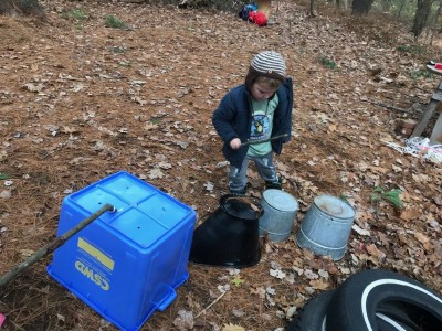 Lijah playing drums on tin buckets in the woods