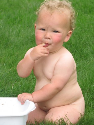 naked Lijah on the grass playing with a tub of water